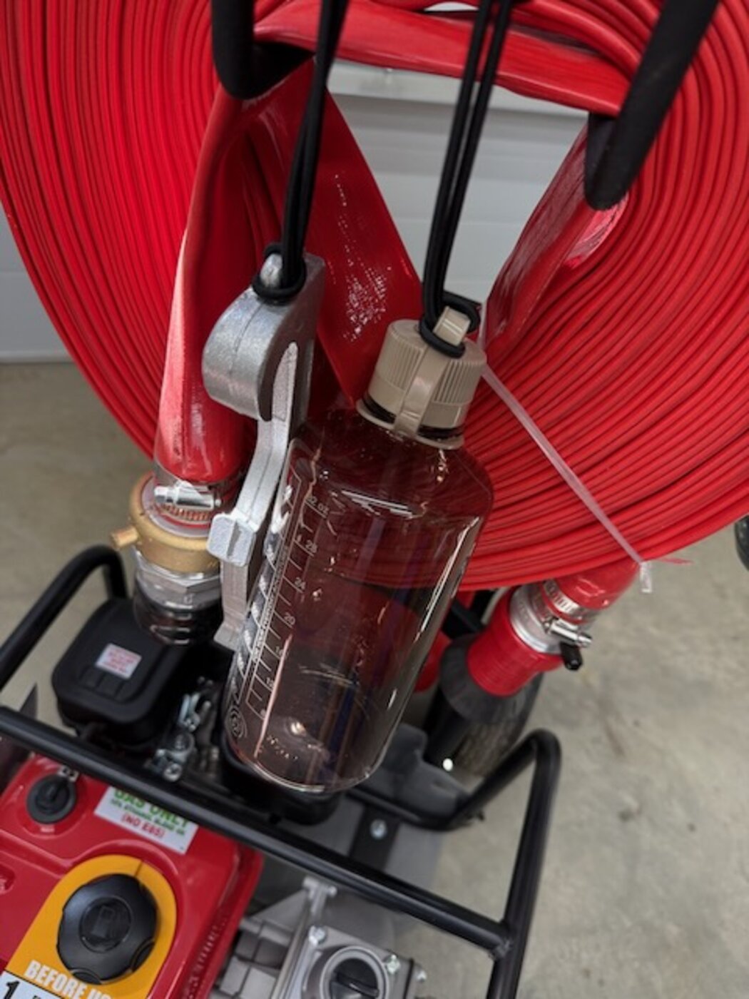 Graduated priming bottle and hose wrench clipped to the FireReady hose reel